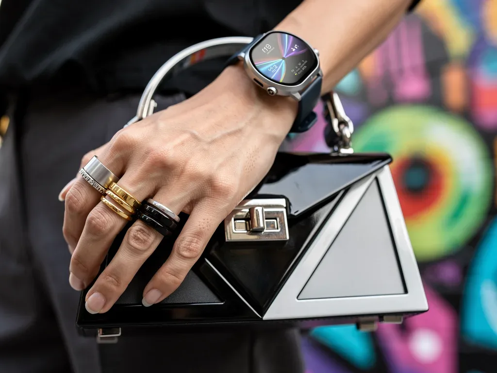 Stylish hand with layered rings, futuristic smartwatch, and structured mini-bag on a street art background